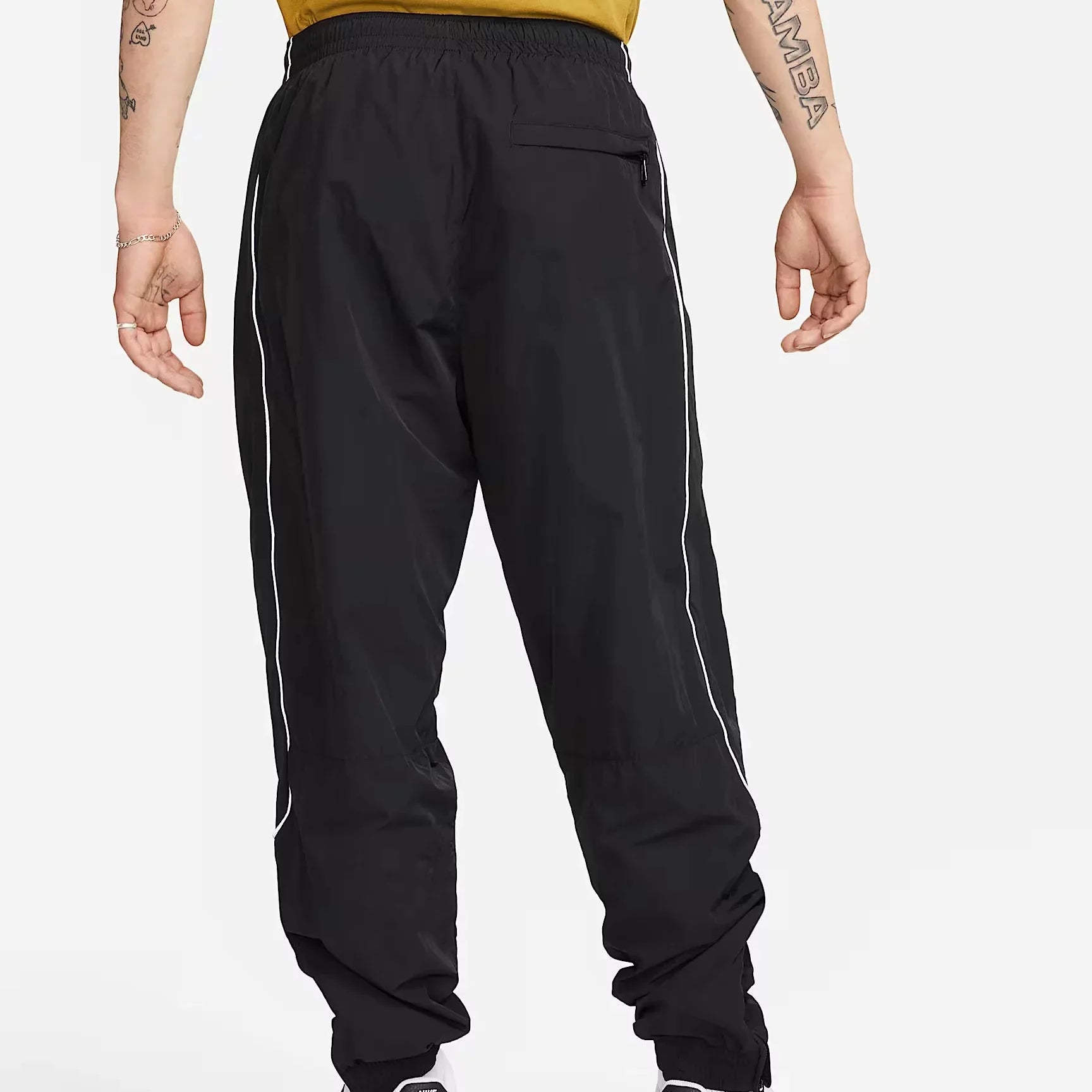 Nike Solo Swoosh Men’s Track Pants in black, back view. Shows secure zip pocket, reflective piping along legs, adjustable cuffs and lightweight nylon fabric.